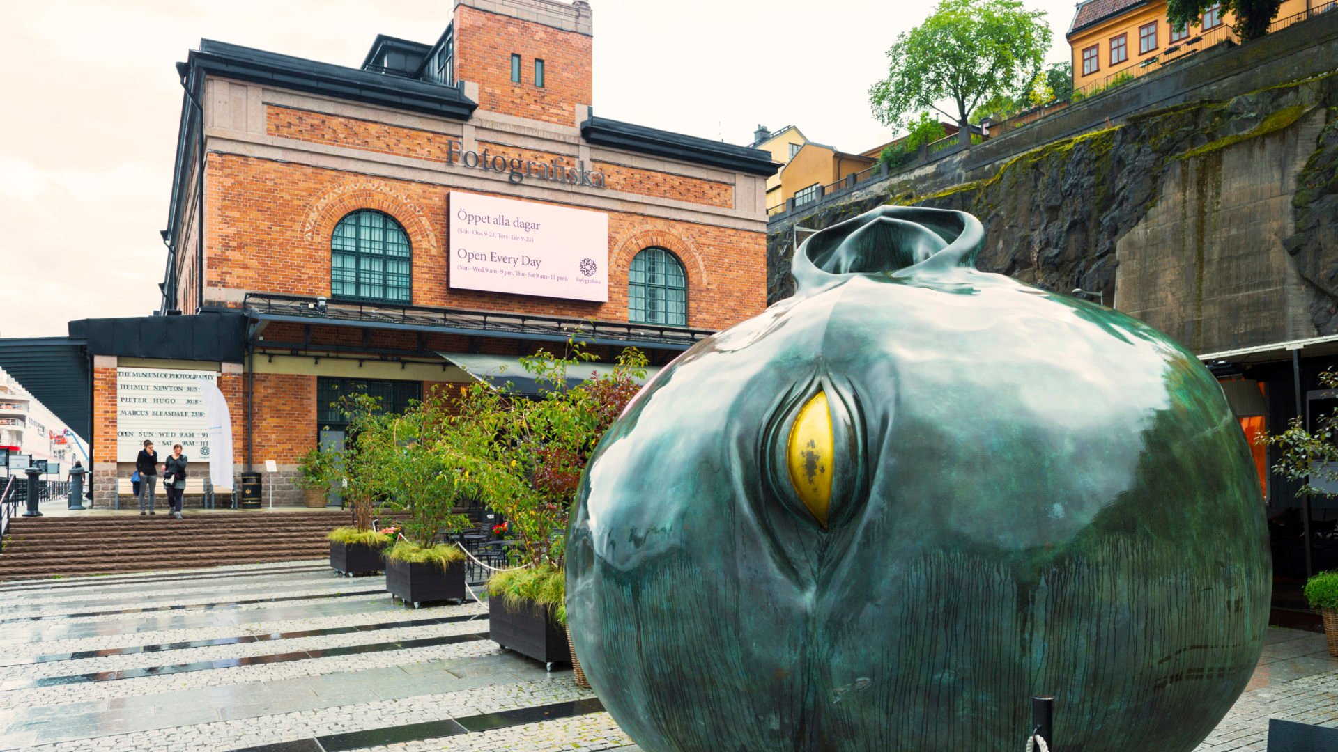 Fotografiskas röda tegelbyggnad med grön rund skulptur med gult öga i förgrunden. Ebab medverkade där i renoveringen i ett CM-projekt.