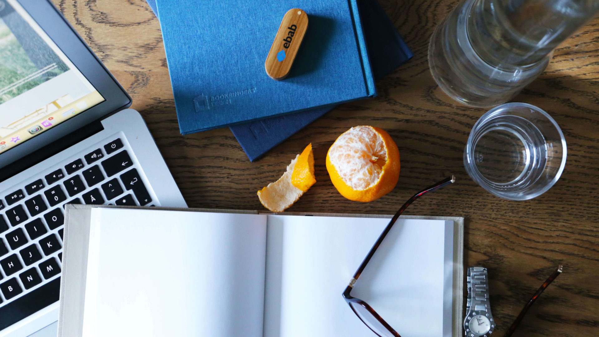 Brunt bord med dator och anteckningsböcker med en skalad apelsin emellan. Affärsutveckling - hitta rätt värden till rätt målgrupp.