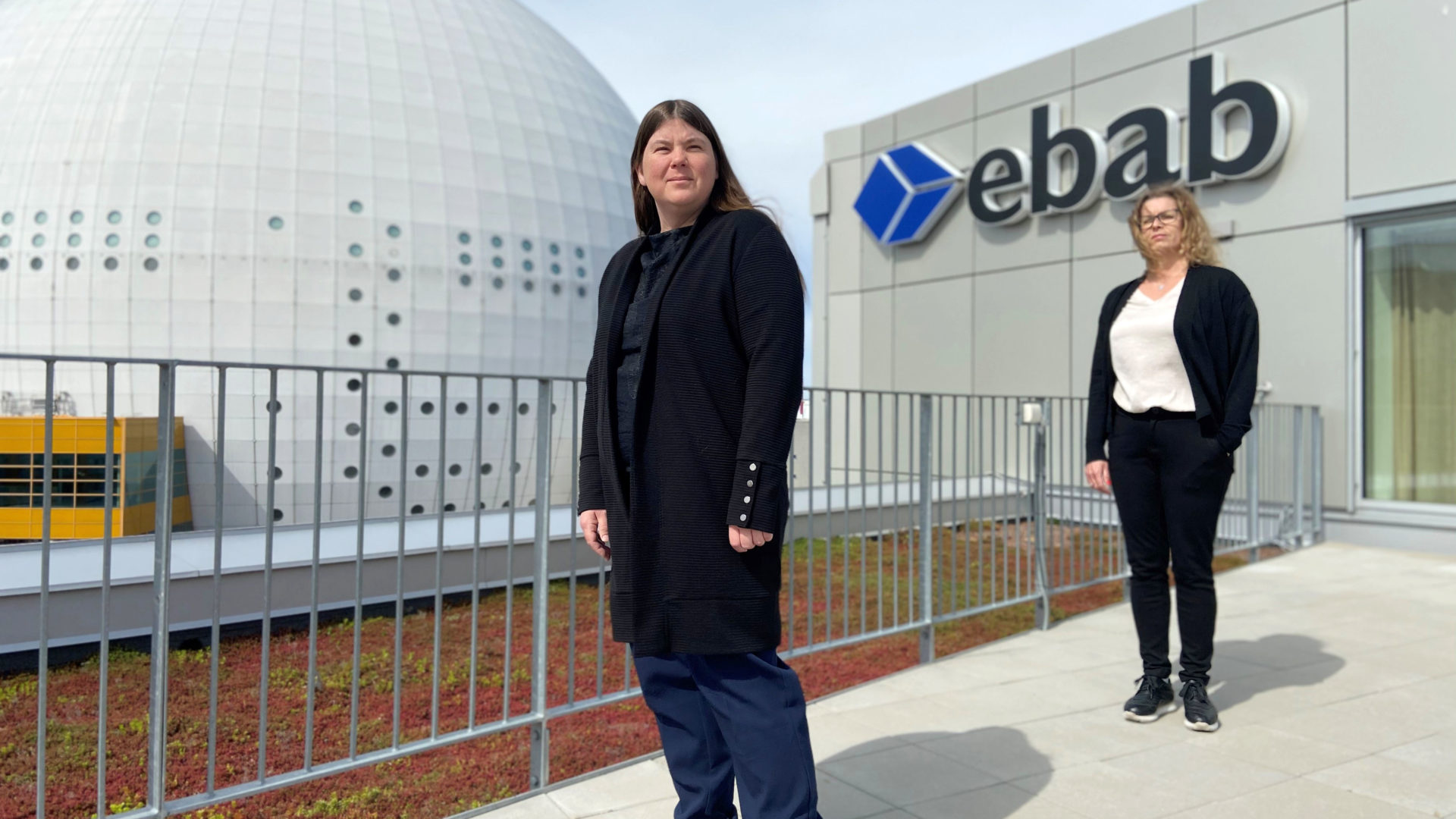 Två kvinnor på en balkong framför en Ebab-skylt med Globen i bakgrunden - Ebab presenterar hållbarhetsrapporten.