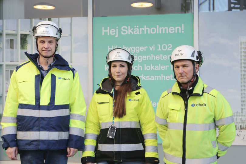 Teamet i Måsholmen med gula reflexvästar och hjälmar framför en skylt med texten Hej Skärholmen! Nya Landmärket i Skärholmen.