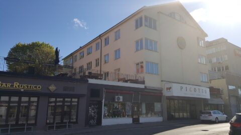 Kortsidan på ett hus i gul puts med verksamheter i nedre botten.