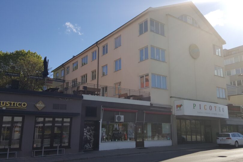 Kortsidan på ett hus i gul puts med verksamheter i nedre botten.